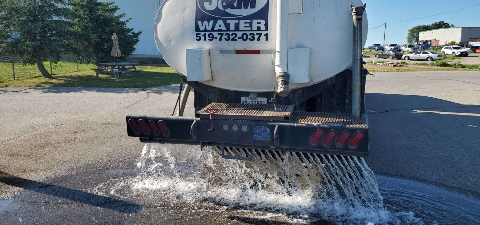 J&M Water Hauling Truck with Spray Bar for Dust Control and Road Construction, spraying water on the asphalt.